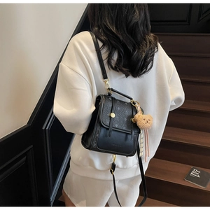 Detail of a black mini backpack with diamond logo prints and a plush bear pendant charm