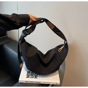 Detail of black crescent canvas bag showing brown leather shoulder pad and metal hardware