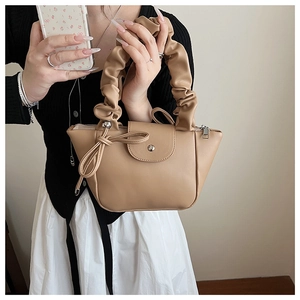 Close-up of pleated cloud handle and bow detail on light brown PU leather handbag