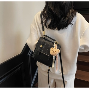 Detail of black textured leather bag with gold hardware and plush bear charm on white sweatshirt