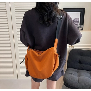 Detail of bright orange nylon crossbody bag featuring black adjustable wide shoulder strap