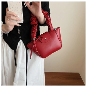Detail of red pleated handbag with bow knot decoration and high-shine PU leather finish