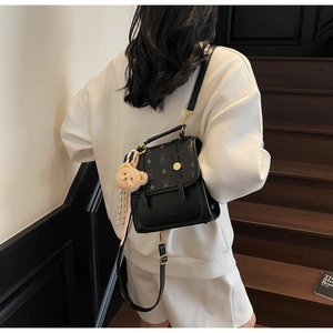 Detailed back view of a black leather mini backpack with patterned flap and plush bear charm