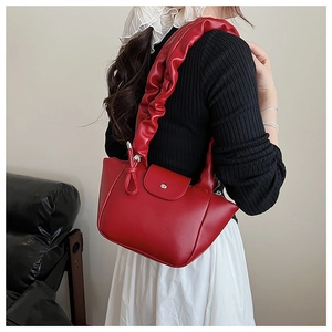 Close-up of a stylish red leather handbag featuring a unique ruched pleated shoulder strap