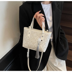 Detail of cream crossbody bag featuring geometric patterns and elegant tassel charm