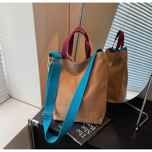 Détail du sac cabas en toile bicolore avec anse bordeaux et bandoulière bleue sur meuble noir