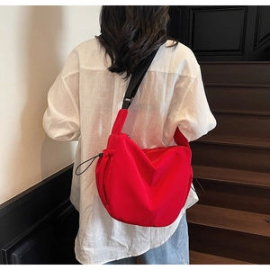 Detail view of large red canvas dumpling bag with black nylon shoulder strap on model