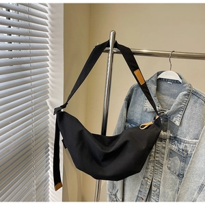 Detail of black canvas crescent bag with adjustable strap and brown leather zipper pull