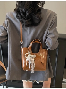 Caramel brown leather bucket bag with pearl lace bow charm worn by a model in a gray blazer