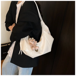 Detail of white pleated patent leather crescent bag with cute pink plush bear charm