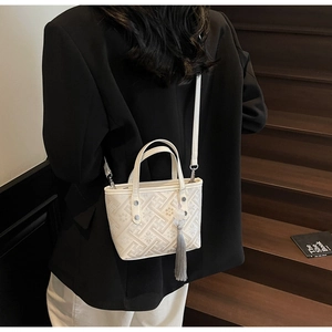 Detail of cream bucket bag featuring geometric embossed patterns and tassel charm
