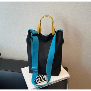 Détail du sac cabas en toile avec poignées jaunes et bandoulière bleue sur livres