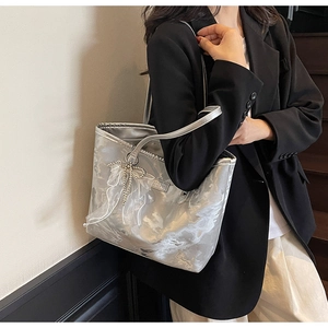 Detail der silbernen Metallic-Tasche mit weißer Netzschleife und Perlenanhänger