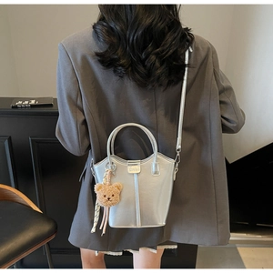 Silver bucket bag detail featuring dual ring handles, plush bear charm, and striped ribbon