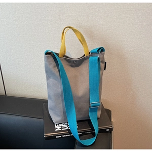 Détail du sac en toile grise avec anses jaunes et bandoulière bleue sur un canapé en cuir