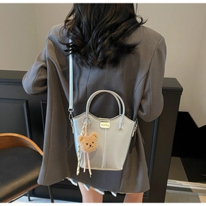 Detailed back view of a silver bucket bag with a cute bear charm on a female model