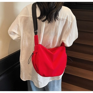 Detail of red dumpling crossbody bag featuring a wide black adjustable shoulder strap
