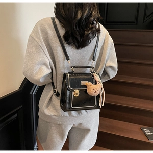 Close-up of black PU leather backpack with gold lock and cute brown bear pendant on stairs