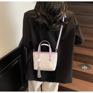 Detail view of woven lilac bucket bag featuring a silk tassel and faux leather straps