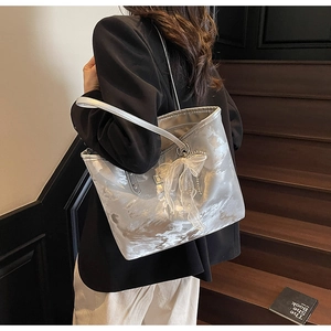 Detail der silbernen Textur-Tote-Bag mit Stoffschleife und Metallkette auf schwarzem Blazer
