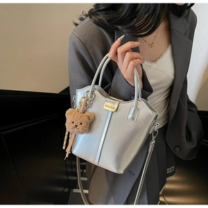 Silver leather bucket bag with vertical stitching and a brown plush bear charm detail