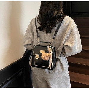 Detail of black vintage PU backpack with gold lock, pearl rivets and plush bear charm