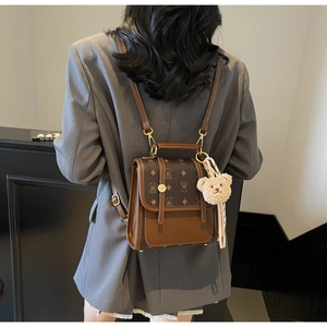 Detailed back view of a retro brown monogram backpack with teddy bear charms on a model