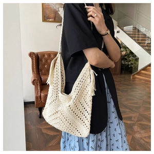 Detail shot of a bohemian cream woven tote bag with long tassels on a vintage leather sofa