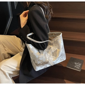 Detail einer silbernen Metallic-Tasche mit durchsichtigem Spitzen-Anhänger auf Holz