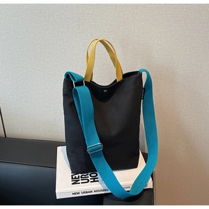 Détail du sac cabas en toile montrant le tissu noir avec anses jaunes et bandoulière bleue