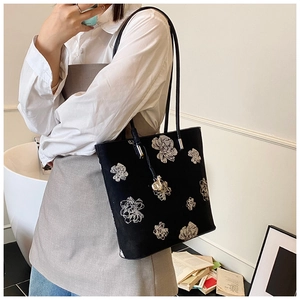 Detail of elegant black tote bag featuring fine floral embroidery and slim leather strap