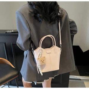 Detail view of pink bucket bag with plush bear charm worn over a gray suit outfit