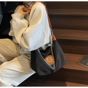 Detail of black crescent bag with metal M logo, orange leather patch, and chain accent
