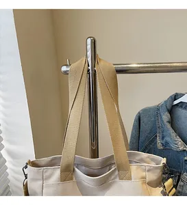 Detail of wide khaki woven strap and beige canvas tote bag with sturdy metal hardware