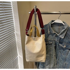 Détail du sac fourre-tout en toile, corps crème, poignée jaune et bandoulière rouge