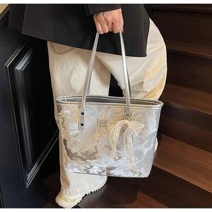 Nahaufnahme der silbernen Metallic-Tasche mit weißer Spitzenschleife und Schultergurt