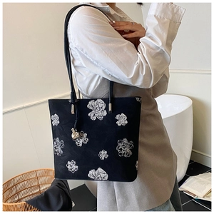 Detail of artistic floral embroidery on black tote bag with silver metal strap hardware