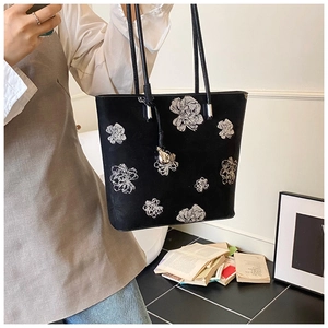 Close-up of black leather tote bag with elegant white floral print and metal charm