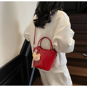 Detail of red leather bucket bag with plush bear charm and crossbody strap