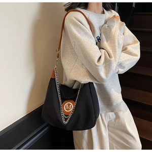 Detail of black nylon crescent bag with silver chain and brown leather M patch logo