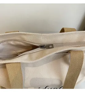 Detail of silver metal zipper closure on a beige canvas tote with brown fabric handles