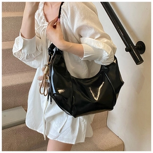 Close-up of glossy black crescent shoulder bag with pleated texture and plush charm
