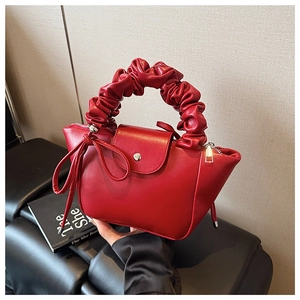 Detail view of red pleated handle bag with delicate texture and magnetic closure