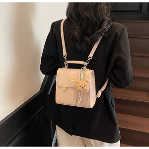 Detail of small beige PU leather backpack with gold clasp and teddy bear charm on a model