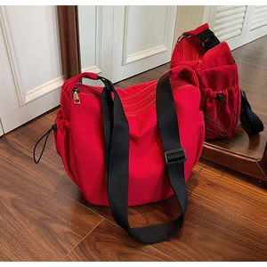 Detail of red nylon crossbody bag showing side drawstring pocket and black strap