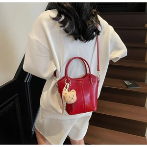 Red glossy leather bucket bag with teddy bear charm shown in a lifestyle indoor setting