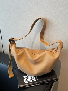 Minimalist khaki canvas half-moon crossbody bag placed on a black leather sofa