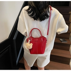 Glossy red bucket bag detail with plush bear charm worn with white outfit on stairs