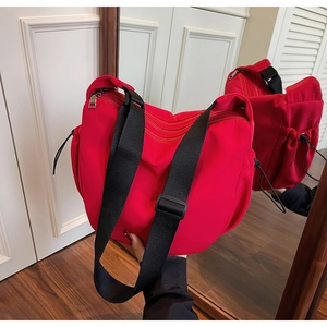 Detail view of large red canvas crossbody bag featuring black straps and drawstring pockets