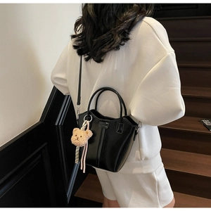 Detail of a shiny black bucket bag with a cute plush bear charm on a shoulder strap